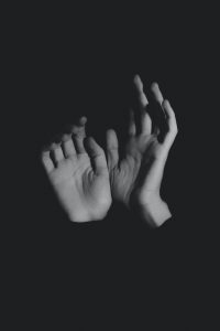 Duas mãos submergem de um fundo completamente escuro.